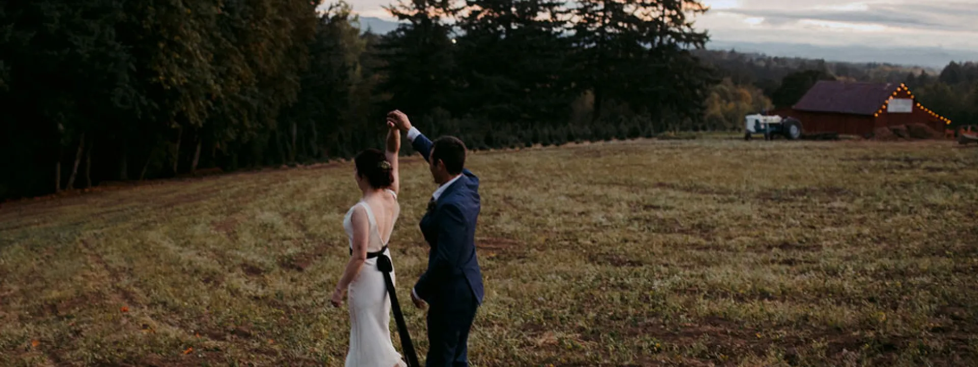 The bride and groom dance in a field at sunset.
